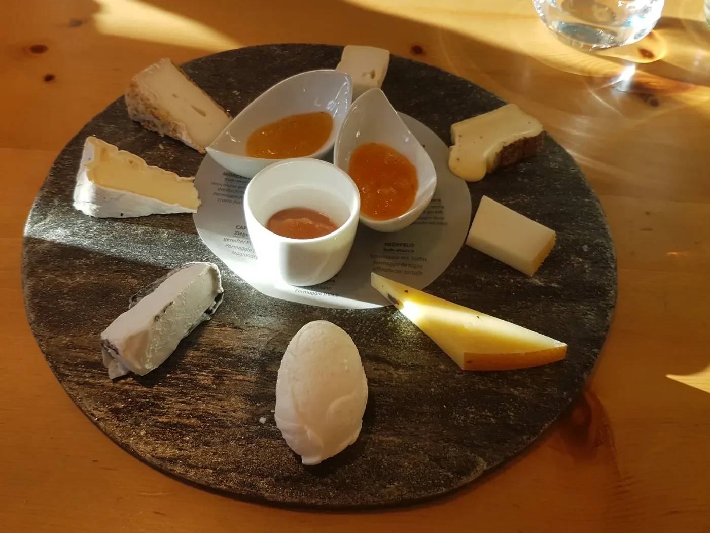 Rundt skiferfat med flere oster og små skåler med gelé og marmelade