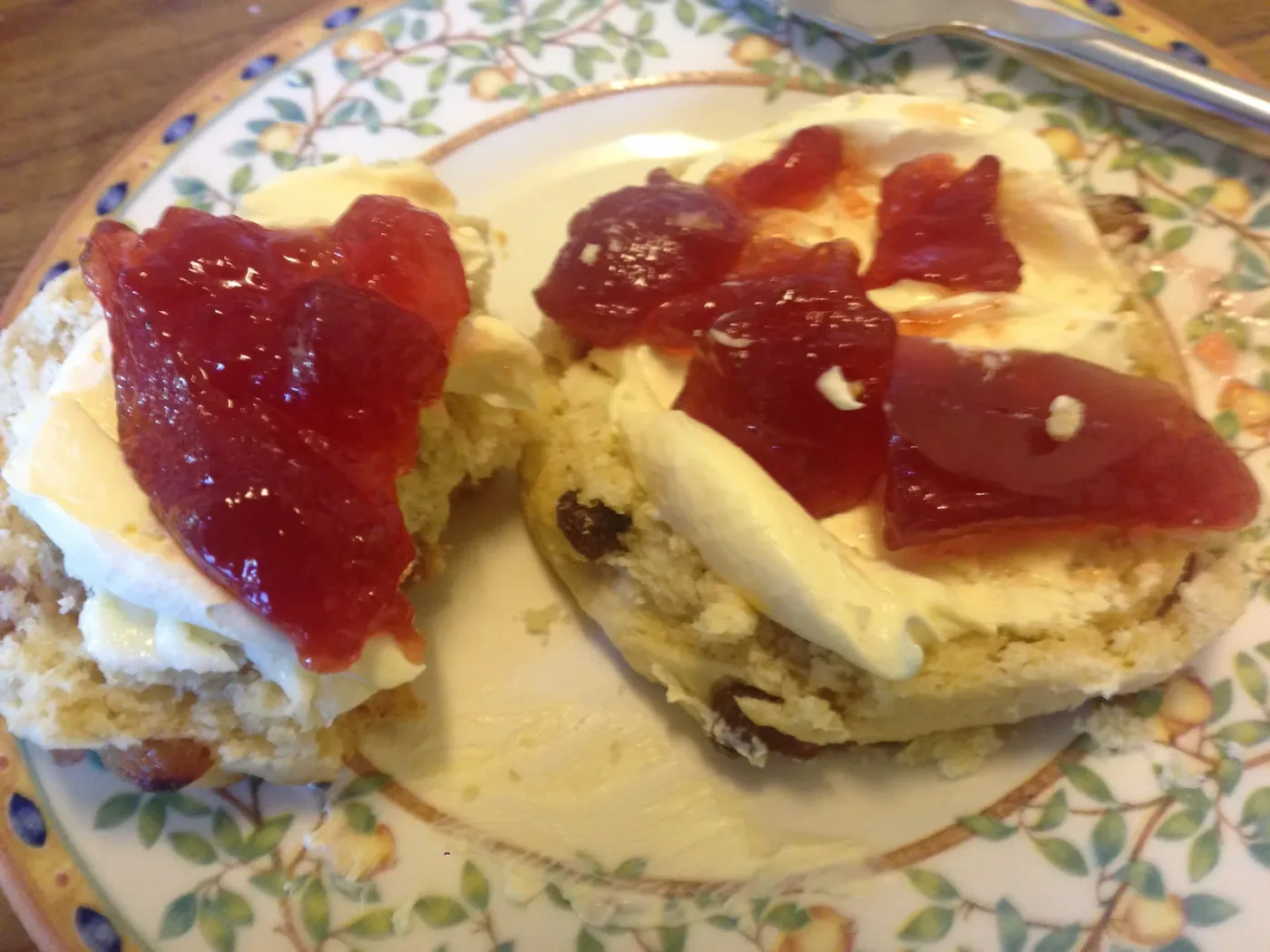 Scones delt i to med tykk krem og jordbærsyltetøy på en blomstret tallerken